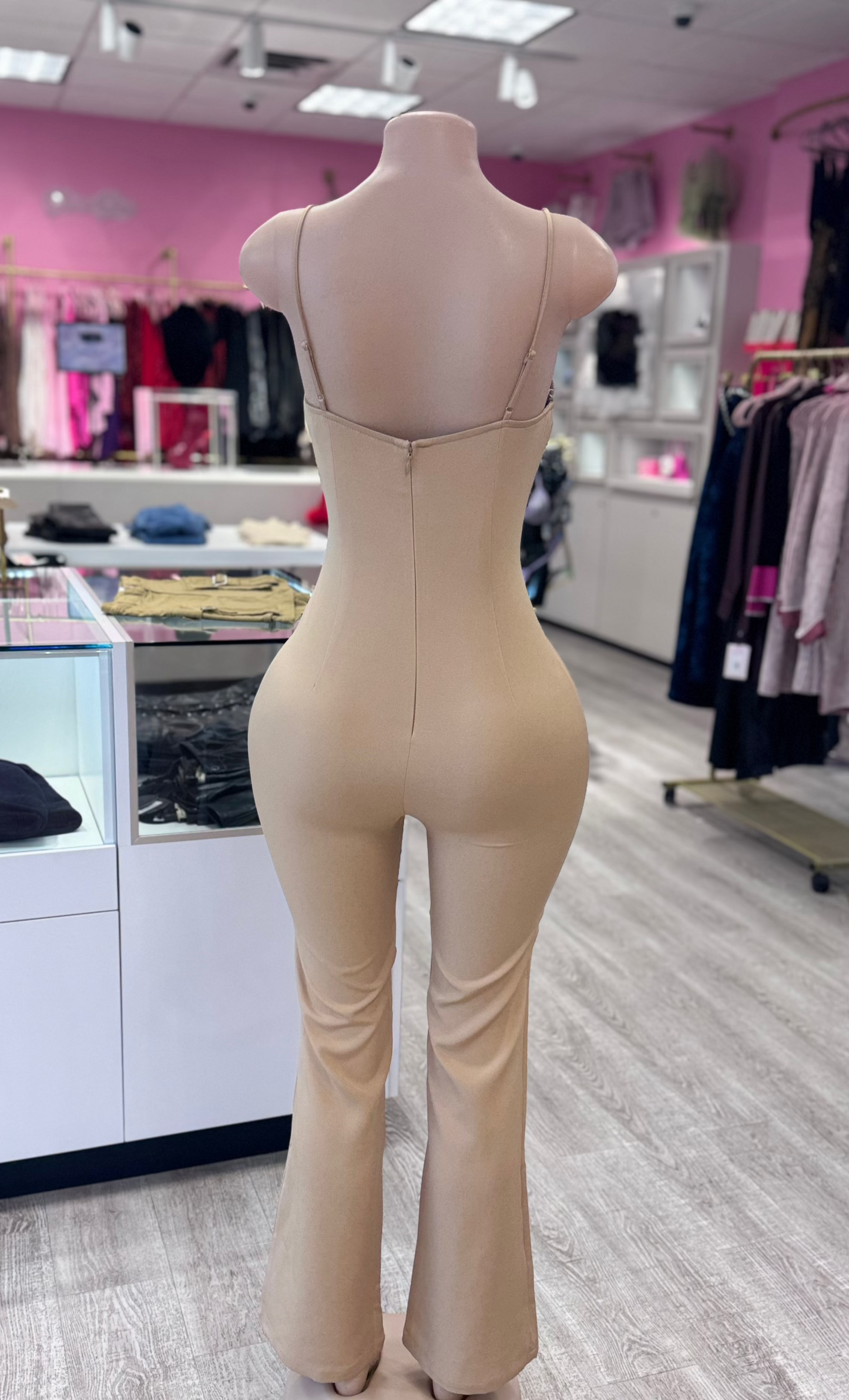 Back view of a sophisticated nude jumpsuit with a sweetheart neckline and zip closure, showcased on a mannequin in a fashionable retail environment, emphasizing its flattering design and versatility.