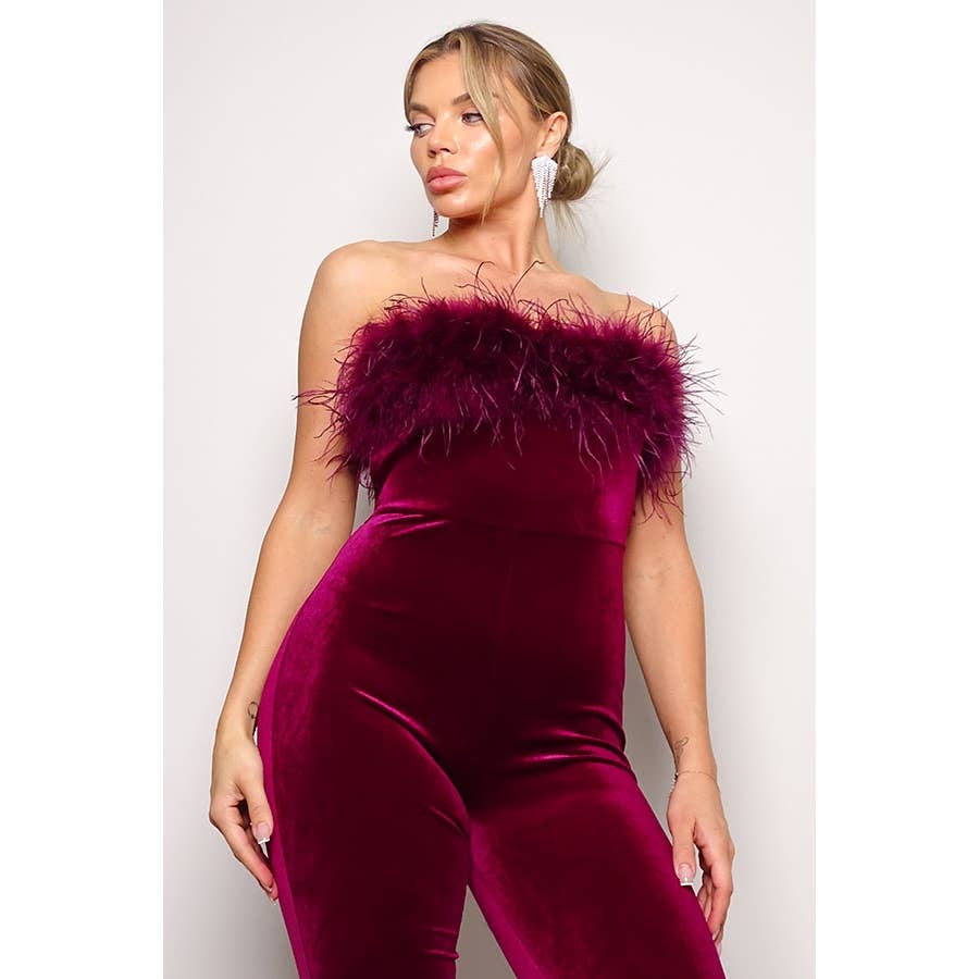 a woman wearing a burgundy velvet jumpsuit with a feather trim