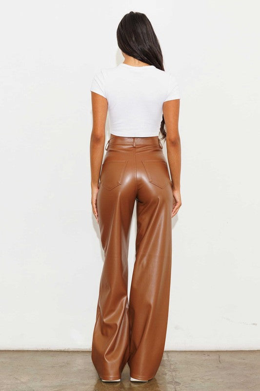 a woman in a white top and brown leather pants