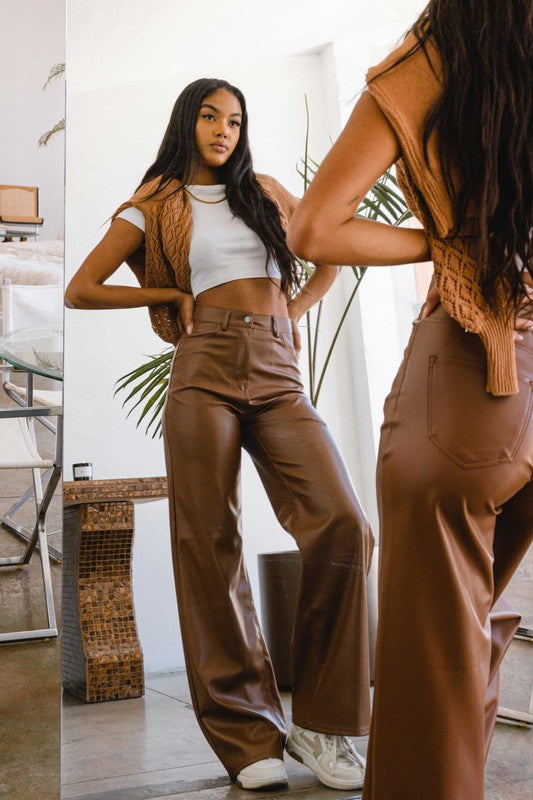 a woman standing in front of a mirror wearing brown pants