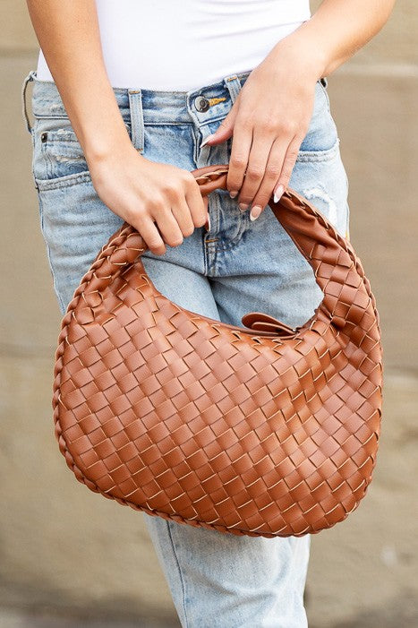 a woman is holding a brown woven purse