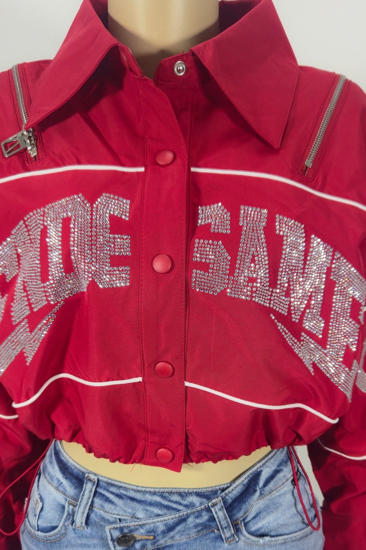 A red cropped button-up crop jacket  silver rhinestones across the front, styled on a mannequin with blue jeans.