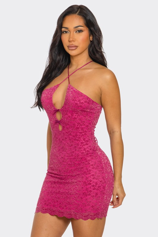 Close-up view of a woman showcasing a stunning fuchsia mini dress with a cutout bow and two circular openings. She stands with a charming smile, accentuating the dress's intricate lace pattern.