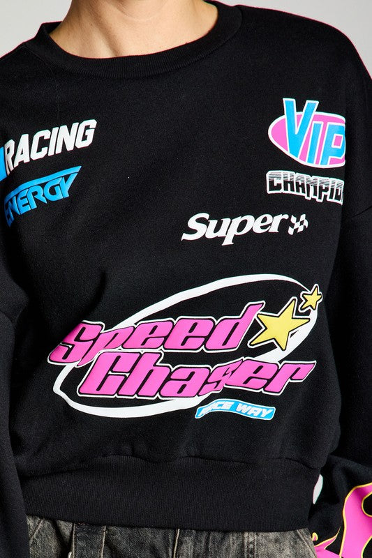 Close-up shot of a black sweatshirt with vibrant branding and graphics, including 'Speed Chaser' in pink. The model is looking down and showcasing the stylish design.