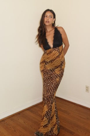 Stylish woman wearing a leopard print maxi dress with a plunging neckline, standing in a bright room.