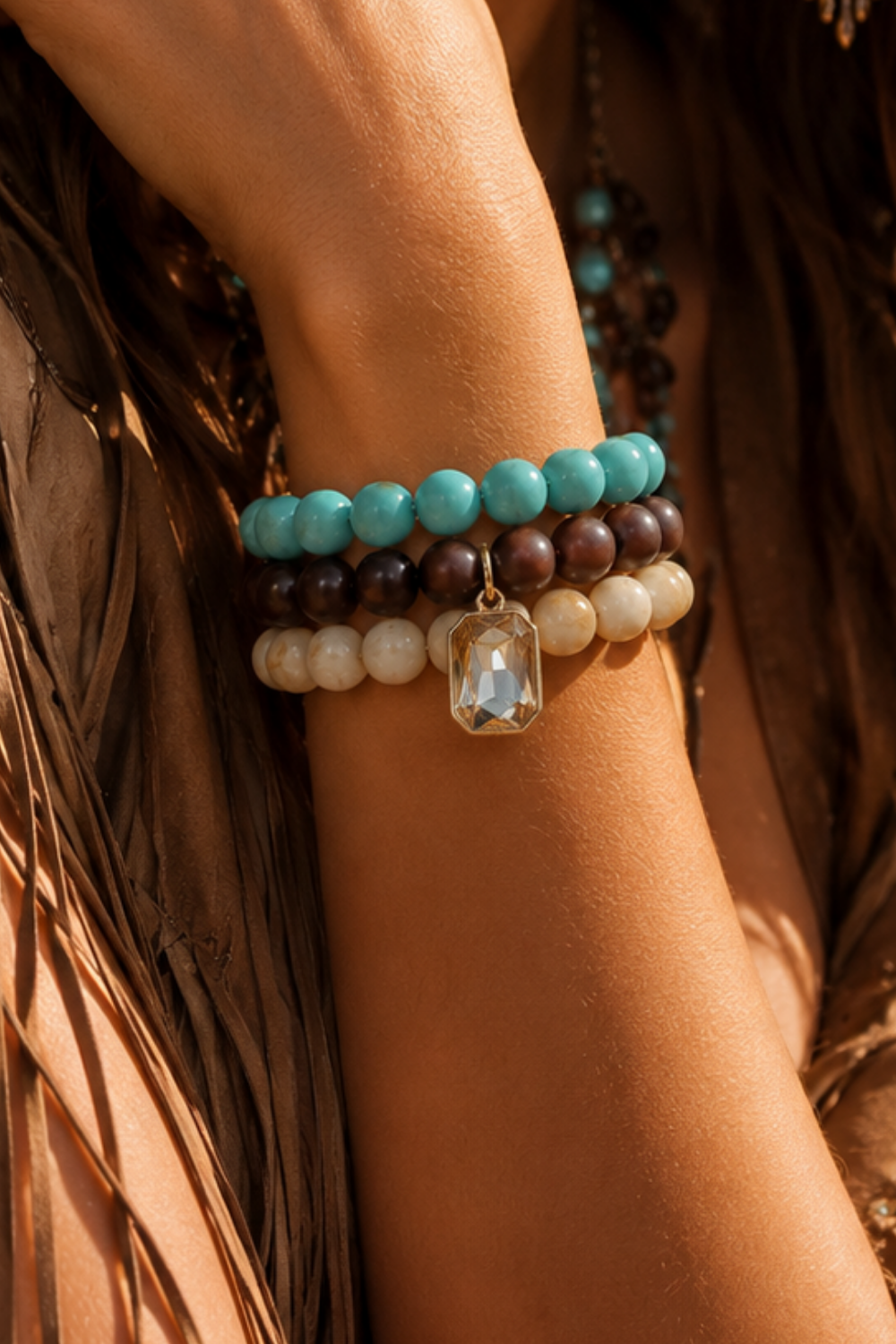 A close-up of a person's wrist wearing a stack of bohemian beaded bracelets. The bracelets feature turquoise, dark brown, cream, and light brown beads with a clear faceted charm.